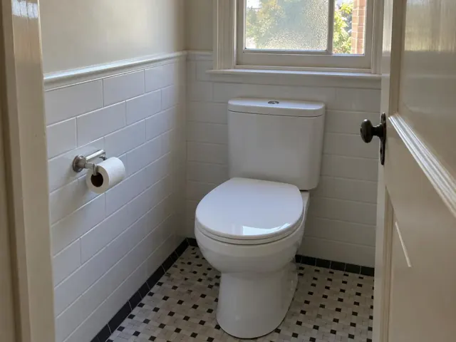 Clean white toilet in a tiled bathroom with a window and mosaic floor in Killara