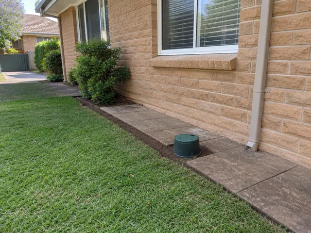 Capped sewer opening beside concrete pavers and brick house wall in St Ives